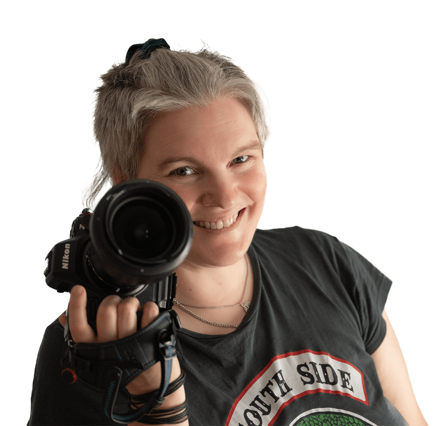 Foto einer Person mittleren Alters, die eine Kamera in der Hand hält und schelmisch grinst.